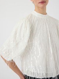 Witte blouse met een hoge halslijn, poffende mouwen en een textuurdesign. Versierd met pailletten en franjes overal.