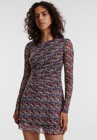 Zwarte bloemenjurk met lange mouwen, gerimpeld detail op het lijfje en een gelaagde zoom, versierd met een mix van kleurrijke bloemen en kleine bladeren.