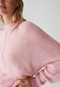 Maglione lavorato a maglia rosa con una vestibilità ampia, maniche larghe a costine e una texture sottile. Presenta un collo alto e un design rilassato.
