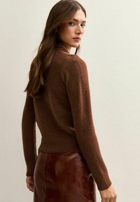 Brown sweater met lange mouwen en een getailleerd ontwerp, gemaakt van een zachte textuur. Draag het over een glanzende bruine leren rok.