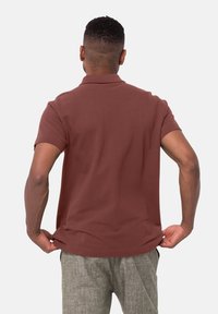 Polo bordeaux en tissu lisse, doté de manches courtes et d'un col classique, associé à un pantalon gris clair texturé.