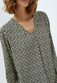 Schwarz-creamfarbenes, gemustertes Blusenshirt mit V-Ausschnitt, langen Ärmeln und einem leichten Stoff, der ein geometrisches Design zeigt.