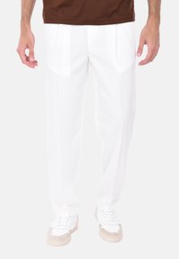 Pantaloni bianchi a pieghe realizzati in tessuto liscio, caratterizzati da un design a gamba diritta e una vita alta, abbinati a sneaker bianche e beige.