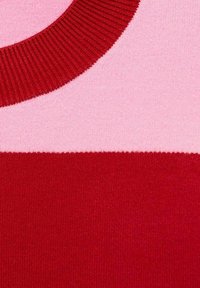 Pull en tricot avec un col rouge côtelé, présentant des sections alternées de rose et de rouge dans une texture lisse. Blocage de couleur géométrique simple.