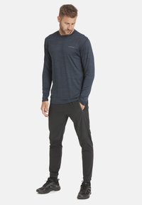 Marineblaue, langärmlige Sportshirt mit subtiler Textur, ausgestattet mit Rundhalsausschnitt und Logo. Kombiniert mit schwarzen, schmal geschnittenen Hosen und schwarzen Sneakers.