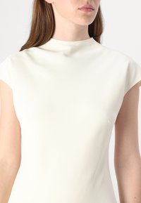 Bela obleka s prilegajočim krojem, visokim ovratnikom in kratkimi rokavi. Narejena iz gladkega, teksturiranega blaga. Minimalističen dizajn brez vidnih vzorcev.