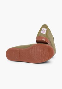 Scarpe di tela verde con suola in gomma testurizzata, caratterizzate da un bordo cucito e un piccolo etichetta cucita di lato.
