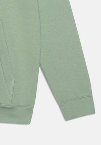 Jasnozielona bluza z miękkiego, teksturowanego materiału, z prążkowanymi mankietami i kieszenią kangurką, prezentująca luźny krój i prosty design.