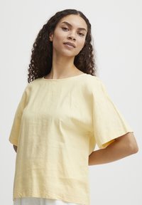 Haut jaune à manches courtes avec un col rond, fabriqu�é en tissu léger. Présente une coupe ample et une texture subtile. Design simple sans motifs.