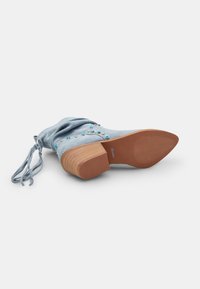 Botín de ante azul con un diseño holgado, tacón de madera, tachuelas decorativas y cordones a juego. Suela texturizada para mayor agarre.