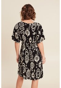 Schwarzes Kleid mit weißen, filigranen Mustern, kurzen Ärmeln, elastischem Bund und einem ausgestellten Rock, aus einem glatten, leichten Stoff.