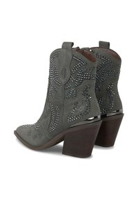 Botas de cowboy de ante gris con punta afilada, adornadas con tachuelas plateadas en patrones florales y estelares, y un tacón marrón apilado.