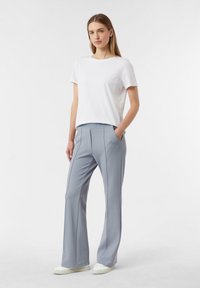 Jasnoszare, dopasowane spodnie z bocznymi kieszeniami i wyraźnym przeszyciem, zestawione z prostą białą koszulką na krótki rękaw oraz białymi sneakersami.