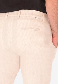 Pantaloni beige chiaro con una delicata trama a righe, dotati di tasca posteriore e una consistenza liscia. Design minimalista con una vestibilità su misura.