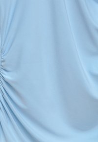 Ljusblå klänning med mjukt, stretchigt tyg och rynkad detalj på sidan som skapar ett flödande, draperat utseende.