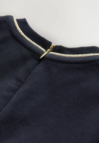 Marine textiel met een zachte textuur, voorzien van een gouden ritssluiting aan de achterkant, aangekleed met een metallic rand langs de halslijn.