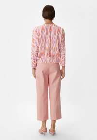 Langermige top met een meerkleurig abstract patroon; gecombineerd met lichtroze cropped broeken en bijpassende open teen hakken.