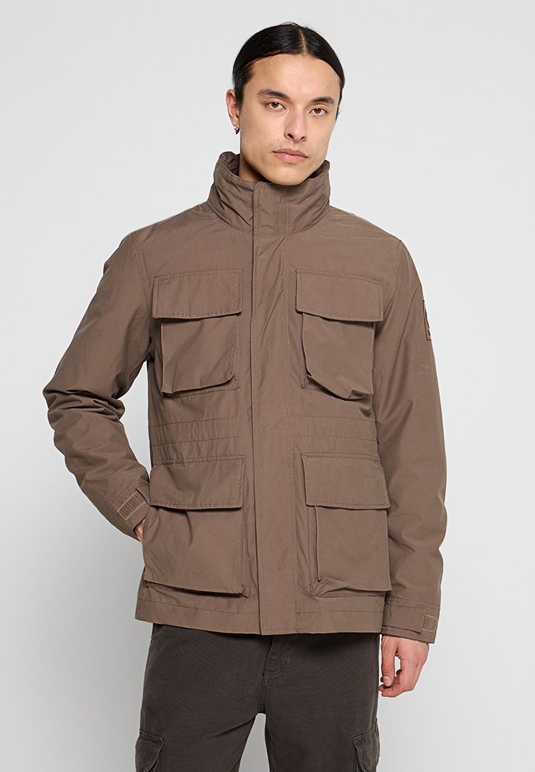 Giacca marrone con cappuccio realizzata in tessuto resistente, dotata di quattro tasche frontali, chiusura con zip e cuciture strutturate per un design funzionale.