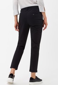Černé, dobře střižené kalhoty s úzkým střihem, vybavené jednou zadní kapsou, manžetami na spodním okraji a hladkou texturou látky. V kombinaci s černými teniskami.