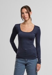Granatowa koszula z długim rękawem, dekoltem w serek, wykonana z gładkiego, elastycznego materiału. Dobrze dopasowana do ciała, podkreślająca sylwetkę.