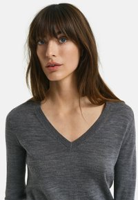Pull en V gris avec manches longues, fabriqué dans un tissu doux et texturé. Présente un col côtelé et des variations de couleur claires et subtiles.