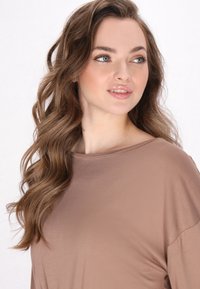 Maglietta marrone, ampia e morbida, con scollatura a barca, texture morbida e maniche lunghe, che presenta una vestibilità rilassata e una caduta fluida del tessuto.