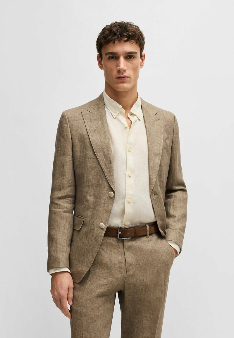 Light brown linen suit with a tailored fit, single-breasted blazer, and flat-front trousers, paired with a beige button-up shirt and brown belt.