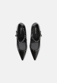 Des chaussures Mary Jane en cuir verni noir avec des bouts pointus, ornées de clous en argent décoratifs sur le haut et d'une sangle à boucle.