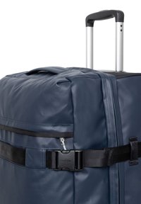 Maleta azul oscuro con ruedas fabricada en material sintético texturizado, que cuenta con un asa retráctil, compartimentos con cremallera y una hebilla negra para la correa.