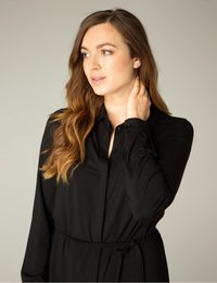 Zwarte langslavige jurk met knoopsluiting aan de voorkant, een ingesnoerde taille en zachte stof. Voorzien van een kraag en een gladde textuur.