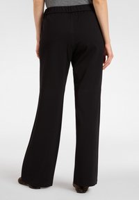 Zwarte wijde broek met een soepele textuur en elastische tailleband, weergegeven vanuit de achterkant. De stof valt zachtjes tot op de grond.