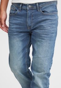 Vidutinio mėlynumo džinsai iš džinso audinio su tiesių kojų kirpimu, penkiomis kišenėmis ir metaliniu mygtuko užsegimu. Išblukusi faktūra su subtiliomis siūlės detalėmis.