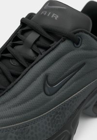 Közelkép fekete és sötétszürke Nike Air sportcipőről, texturált felsőrésszel, fűzős kialakítással és fényes Nike swoosh logóval az oldalon.