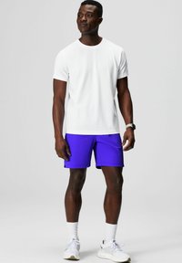 White short-sleeve T-shirt paired with purple athletic shorts. The outfit is completed with white athletic shoes and crew-length socks.