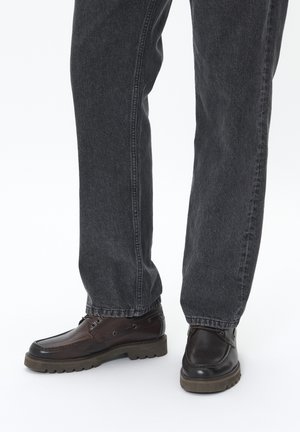 Braune Lederschuhe mit einer strukturierten Oberfläche, runder Zehenpartie und geriffelter Gummisohle, getragen zu dunkelgrauen Denim-Jeans.