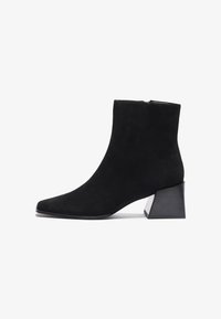 Bottes cheville en daim noir avec un bout pointu et un talon bloc distinctif. La texture est lisse, et le talon présente un design géométrique.