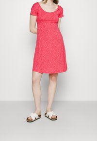 Rotes Blumenkleid mit kurzen Ärmeln, Rundhalsausschnitt und ausgestellter Silhouette, kombiniert mit weißen Crossover-Sandalen.