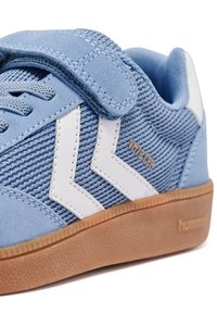 Helle blaue Sneaker mit strukturiertem Stoff und Wildleder-Akzenten. Besitzt ein weißes Chevron-Design, einen Klettverschluss und eine Sohle aus Gummirubber.