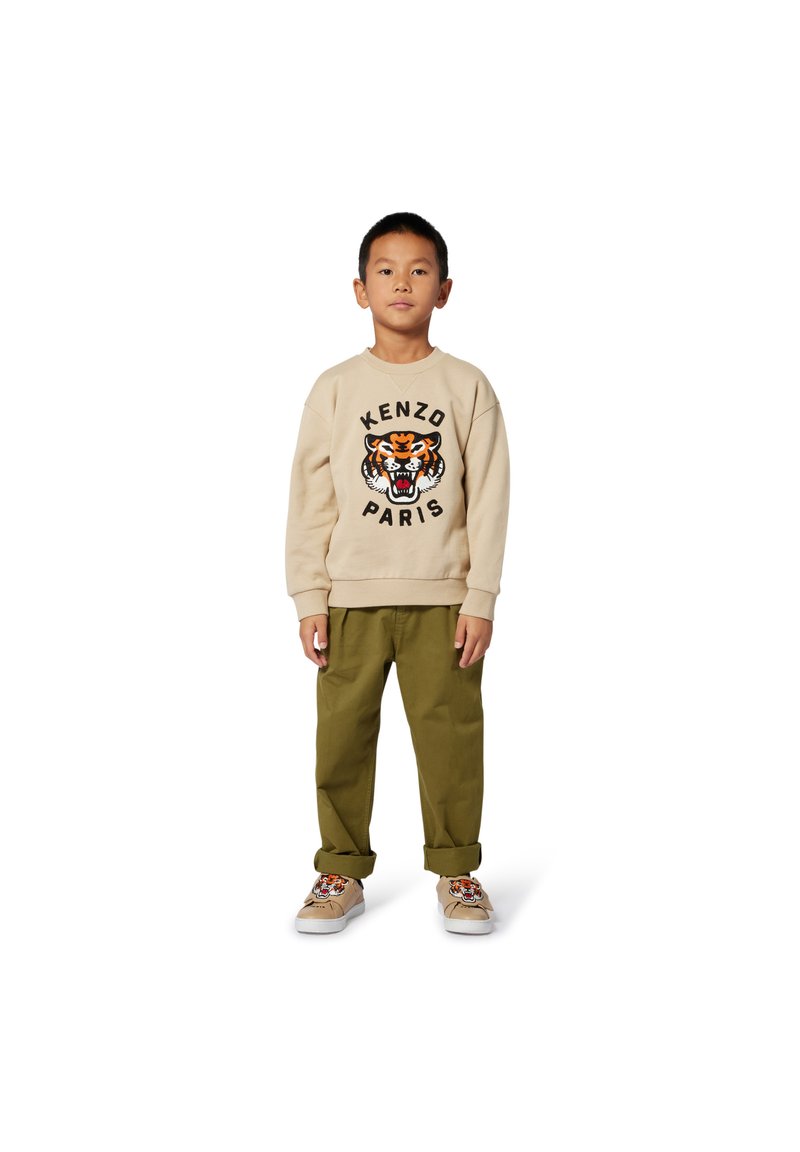 Sweat-shirt beige avec un motif de tigre et le texte "KENZO PARIS", associé à un pantalon vert olive et des chaussures beiges avec un design de tigre.