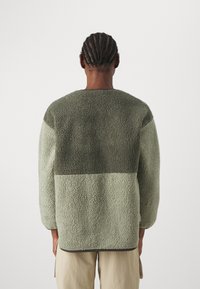 Pull en polaire dans deux nuances de vert, surface texturée, coupe décontractée, col rond et bordures contrastantes le long des bords.