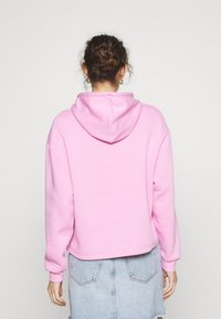 Sudadera rosa corta con capucha ajustable, hecha de tela suave. Cuenta con mangas largas y puños acanalados. Combinada con una falda de mezclilla clara.
