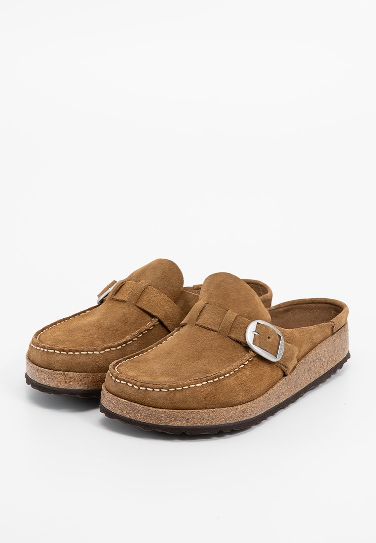 Brązowe zamszowe klapki na płaskiej podeszwie z regulowanymi klamrami, ozdobnym przeszyciem, korkowymi wkładkami i czarnymi teksturowanymi podeszwami.