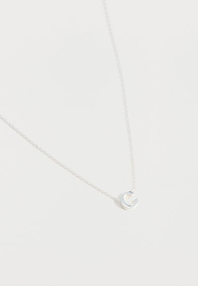 Collier fin en chaîne argentée avec un petit pendentif circulaire lisse et ouvert reposant sur un fond blanc.