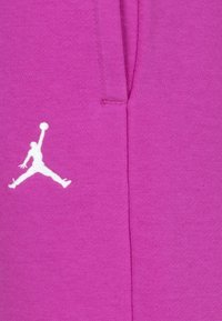 Fukšijas krāsas sporta bikses mīkstā audumā ir apveltītas ar baltu Jordan logotipu. Dizainā ir iekļauta kabata ar rāvējslēdzēju un teksturētas šuves detaļas.