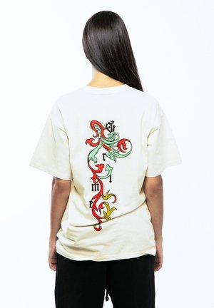 Camiseta de algodón beige con un colorido diseño gráfico en la parte posterior que presenta acentos rojos, verdes y amarillos. Mangas cortas y corte relajado.