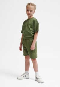 Olivgrön bomullstårt och shorts-set med en liten logotyp-patch. Komplett med vita sneakers och ankelsockor.