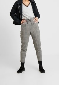 Graue karierte Hose mit elastischem Bund und Zugband, kombiniert mit einem grauen Pullover und einer schwarzen Lederjacke. Schwarze Stiefeletten.