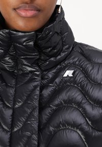 Schwarze Pufferjacke mit hohem Kragen, ausgestattet mit gesteppten Wellenmustern, glänzender Textur und einem kleinen Logo auf der Brust.