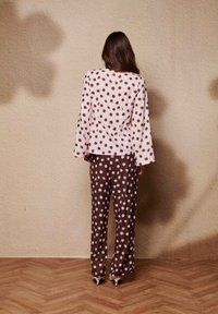 Haut à manches longues à pois dans un rose pâle avec des pois marron, assorti à un pantalon marron présentant le même motif. Tissu lisse, coupe décontractée.