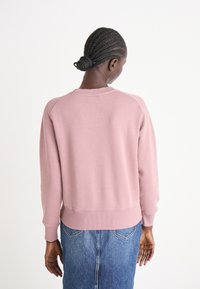 Sweatshirt rose avec des poignets et un ourlet côtelés, doté d'un col ras du cou classique et d'une coupe décontractée. Porté par-dessus une jupe en denim, cela montre une simplicité.